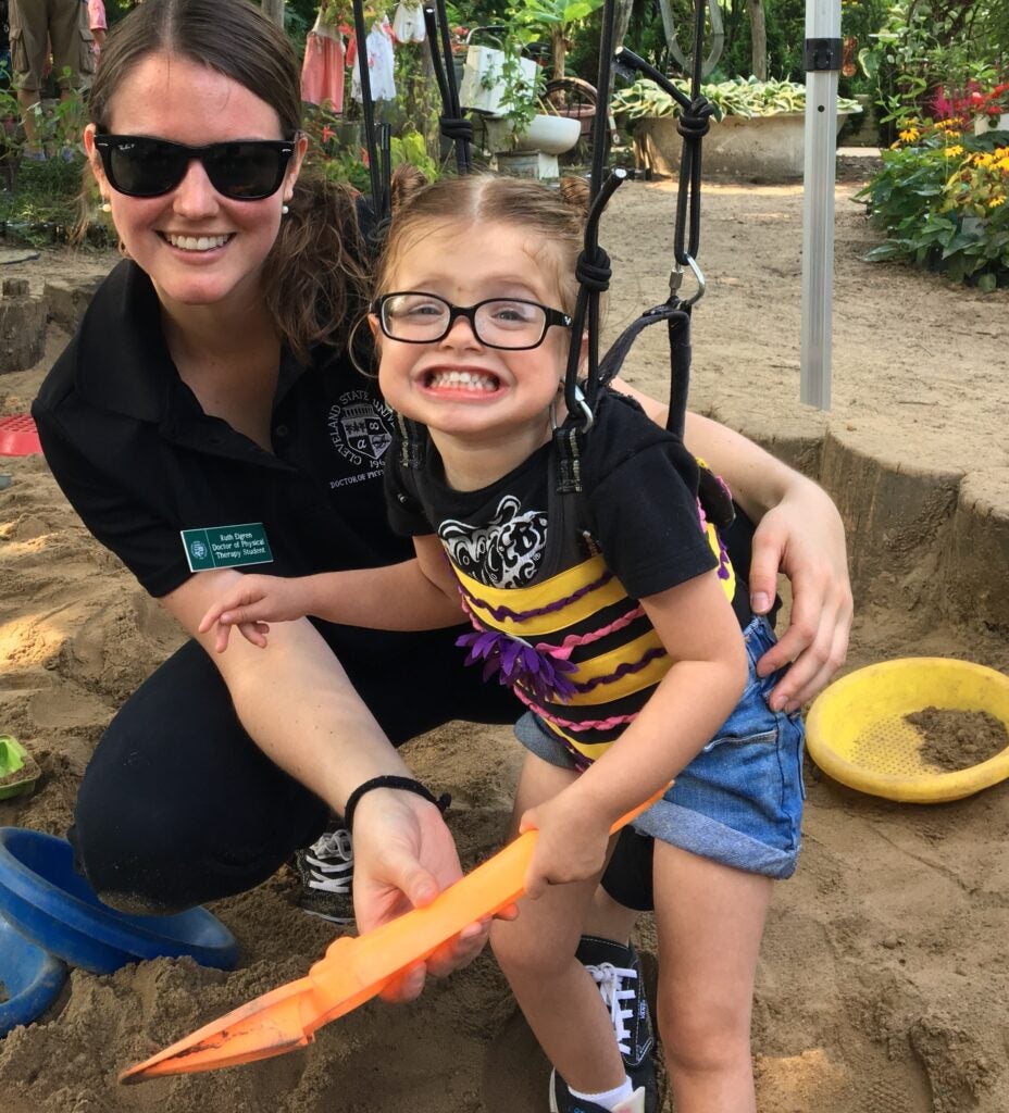 Child holding a sand toy with a volunteer in a sand box.